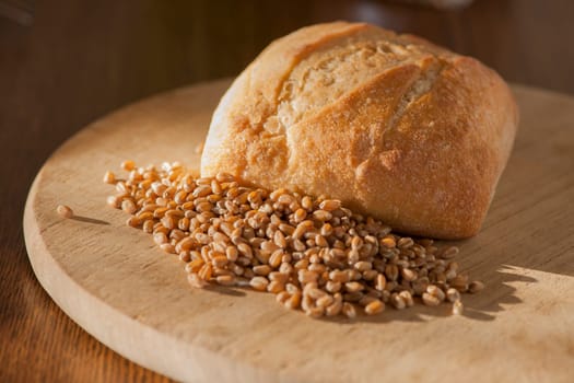 Single roll with spelt grains in front of it on a round breakfast board in the side light.