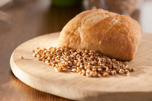 Single roll with spelt grains in front of it on a round breakfast board in the side light.