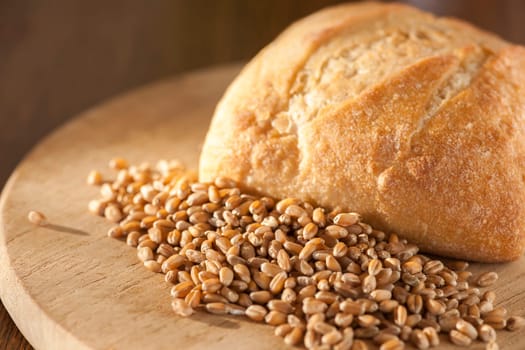 Single roll with spelt grains in front of it on a round breakfast board in the side light.