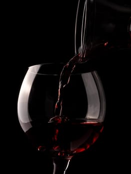 Glass of red wine with an old rustic decanter on a dark background