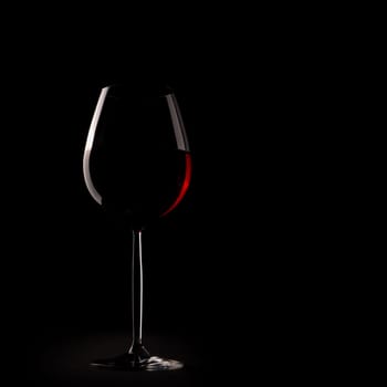 Silhouette of a glass of red wine on a dark table cloth with dark background