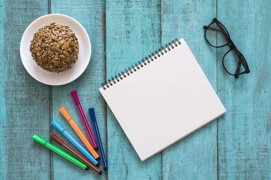 Blue wooden desk table with notebook, color pen, bread and cup of coffee. Top view with copy space, flat lay.