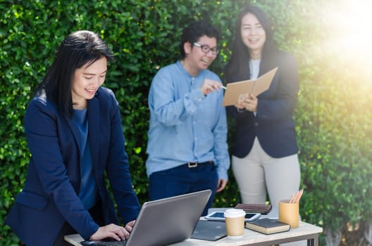 Leader business women concept. Asian business woman using computer laptop and her team dicussing something while working.
