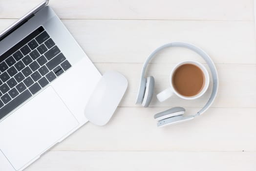 Laptop computer on white table with headphone and coffee cup. View from above