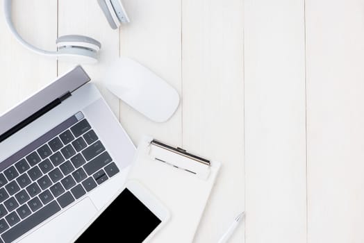 Laptop computer on white table with headphone and smartphone. View from above