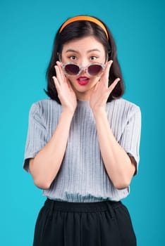 Smiling asian woman dressed in pin-up style dress wearing eyeglasses over blue.