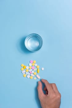 Colored pills in hand with water on blue background.