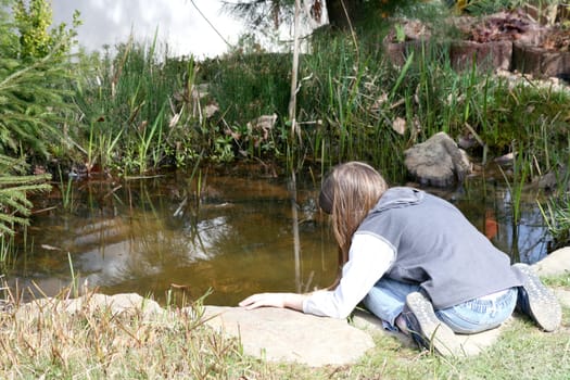 Blonde girl plays on the rocky shore of a lake.