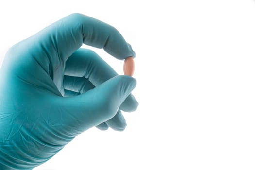 Hand with green protective glove holding an oblong pill, isolated on white background