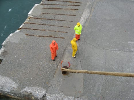 Island of Andros, Cyclades, Greece - September 12, 2009: Three men in wet work protective suit standing on the dock waiting for permission to release ship mooring ropes
