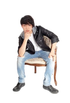 A young Asian man in a black leather jacket sitting in an old armchair.bending forwards with hand on chin, isolated for white background..
