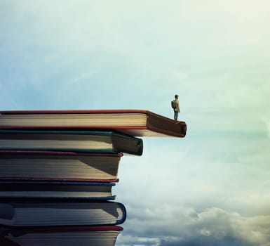 Young boy with a bag on his back stand on a stack of books looking far at horizon. In search of knowlegde concept.