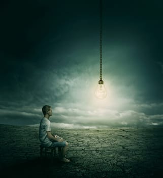 Creative idea concept with a man sitting on a chair in the middle of a desert, looking at a lightbulb