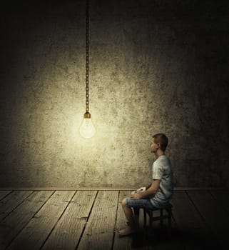 Creative idea concept with a man sitting in a dark room, looking at a lightbulb