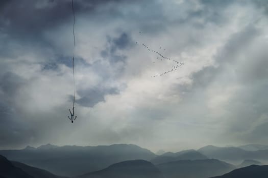 Young man falling from the sky with a rope tied to his leg as safety insurance. Base jump, mysterious crash, life risk and hard determination concept.