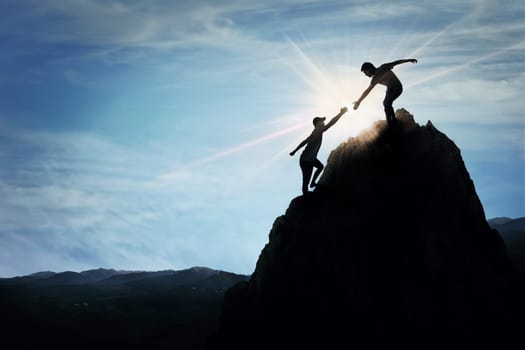 Silhouette of helping hand between two boys climbing a rocky dangerous cliff. Friendly hand on the high mountain hike. Inspirational teamwork, faith and support symbol.