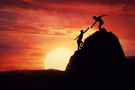 Hikers climbing on rock, mountain at sunset, one of them giving hand and helping to climb. Friendly assistance and support  in a dangerous situation.