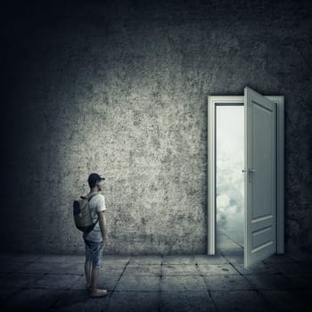Abstract idea with a person standing in a dark room, in front of a opened door. Escape opportunity, entrance to another world.