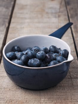 Fresh organic blueberries in a rustic blue bowl on old wooden plank