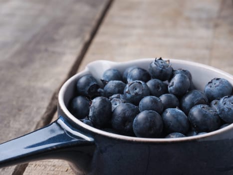 Fresh organic blueberries in a rustic blue bowl on old wooden plank