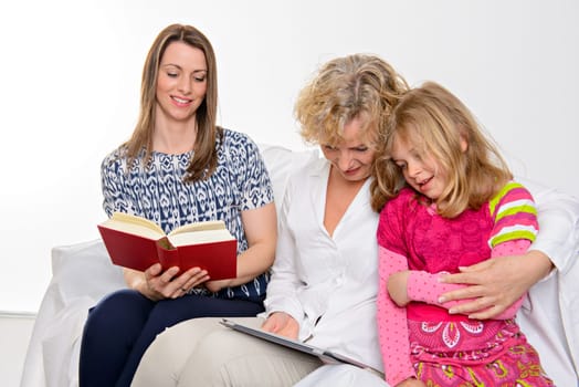 woman with daughter and grandchild together reading in book and tablet PC in front of white background