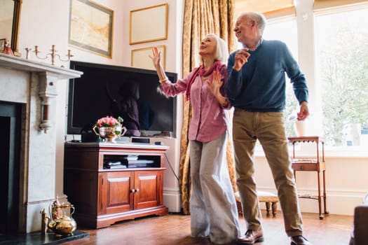 Senior couple are enjoying a dance in the living room of their home.