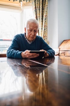 Senior man is sitting at his kitchen table in his home, looking sadly at a picture frame in his hands.