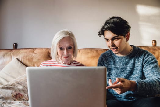 Teenage boy is showing his grandmother how to use a laptop.