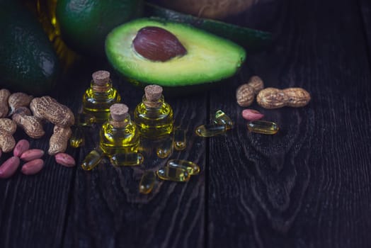 Oil of avocado with fish oil pills and peanut - source of omega 3 on a dark wooden background