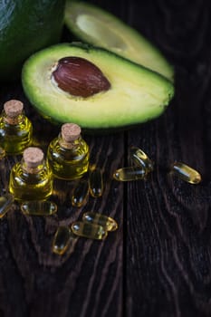 Oil of avocado with fish oil pills on a dark wooden background