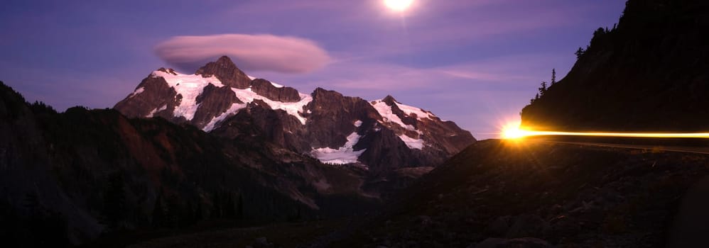 The moon lights up the mountainside as a car creates light streaks in this long exposure