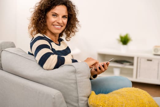 Beautiful woman sitting on the sofa and laughing while sending a text message