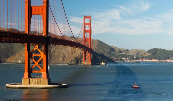 A pilot boat awaits a large cargo ship to enter the bay under the Golden Gate Bridge in San Francisco at dusk