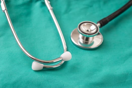 Medical Stethoscope lying on the hospital's green background. The background can be a textile part of a doctor or nurse's work uniform