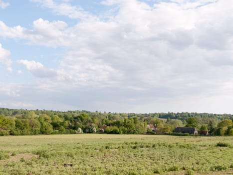 open farmland with houses in the distance outside in the country in essex england dedham in the uk on a bright a sunny day with lots of lush green looking beautiful