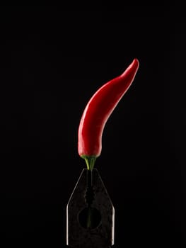 Old rusty pliers holding a red pepperoni on a dark background