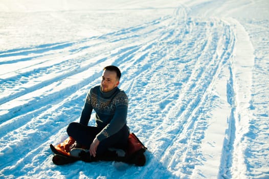 man in warm sweater with a beard is walking on the street in the winter in a warm sunny day, sitting on a snowy road