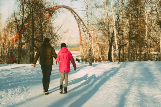 man walking in a winter park with a girl in the background of the bridge
