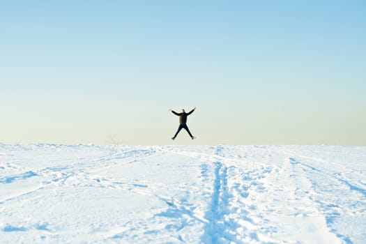 man in warm clothes with a beard is walking on the street in the winter in a warm sunny day at the river against the sky, jumping up and running in the snow