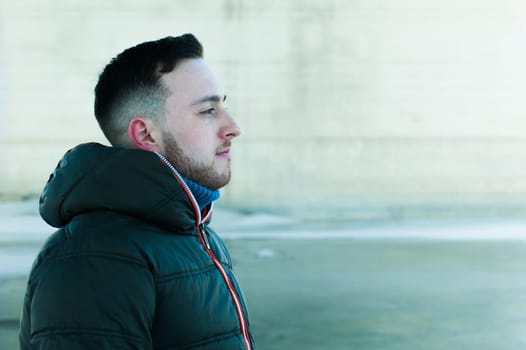 man in warm clothes with a beard is walking on the street in the winter in a warm sunny day at the river bridge in the background