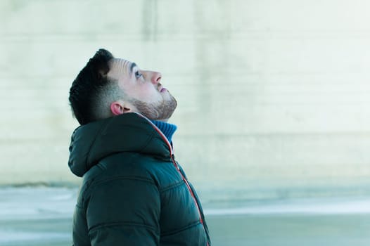 man in warm clothes with a beard is walking on the street in the winter in a warm sunny day at the river bridge in the background