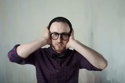 studio portrait of a young man hipster. Guy with beard wearing glasses, hat and a plaid shirt, grabbed his head