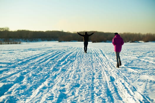 man in warm sweater with a beard is walking on the street in the winter in a warm sunny day, walking along a snowy road with a girl, arms up, rejoicing