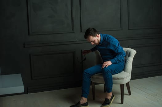 studio portrait of a young man on a dark wall background in a blue shirt and jeans. hipster man, dressed stylishly, with a beard