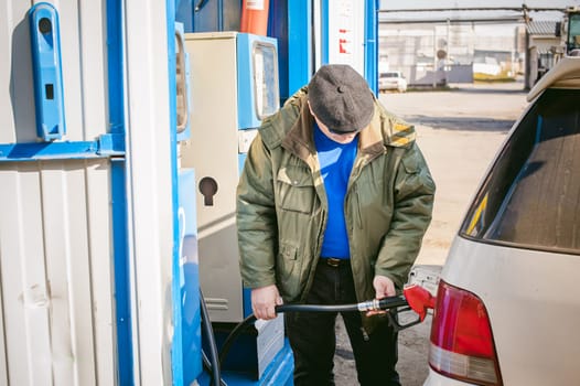 man at a gas station fills the fuel in the vehicle tank. adult man with a mustache and glasses, fueling car before a long journey on the road to non-network gas station
