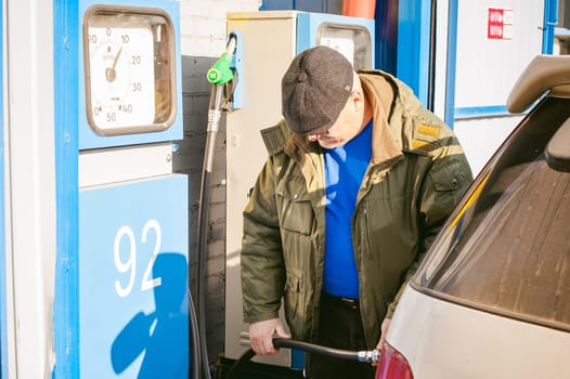 man at a gas station fills the fuel in the vehicle tank. adult man with a mustache and glasses, fueling car before a long journey on the road to non-network gas station