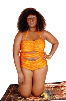 A young African American woman kneeling on a towel on the floor in a orange.bikini, isolated for white background..