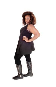 A full body picture on an African American woman in boots and a black.dress standing isolated for white background in profile..