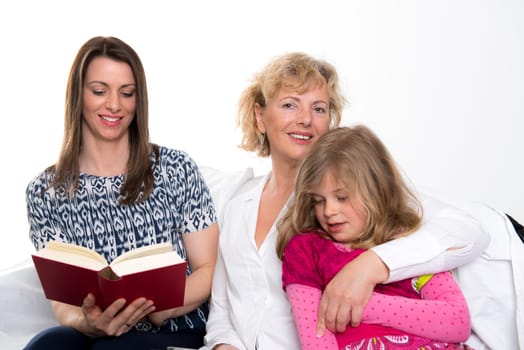 woman with daughter and grandchild together reading in book in front of white background