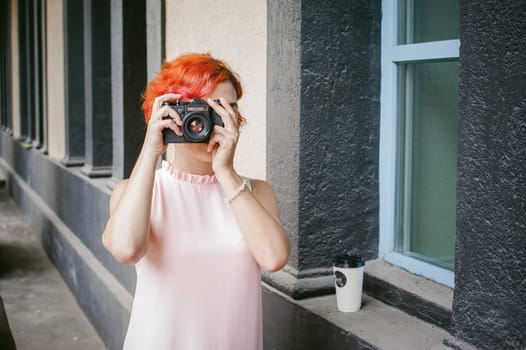 portrait of a girl with a camera. woman with dyed red hair in a pale pink dress derzhet holding vintage camera